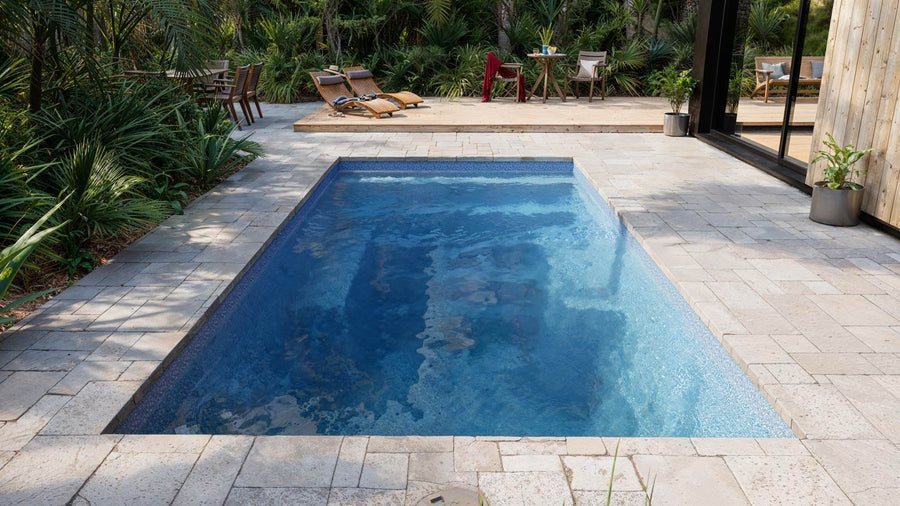 A still fiberglass pool at first light with stone decking and low planting