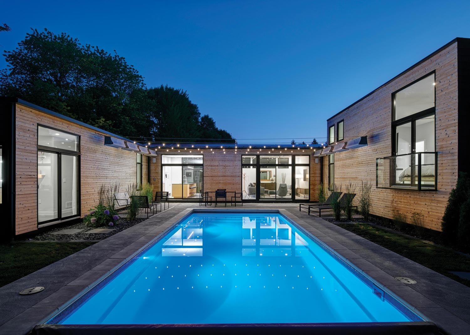 A contemporary rectangular fiberglass pool with still water, stone decking and restrained planting at first light