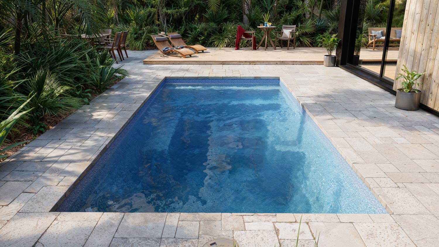 A still fiberglass pool at first light with stone decking and low planting