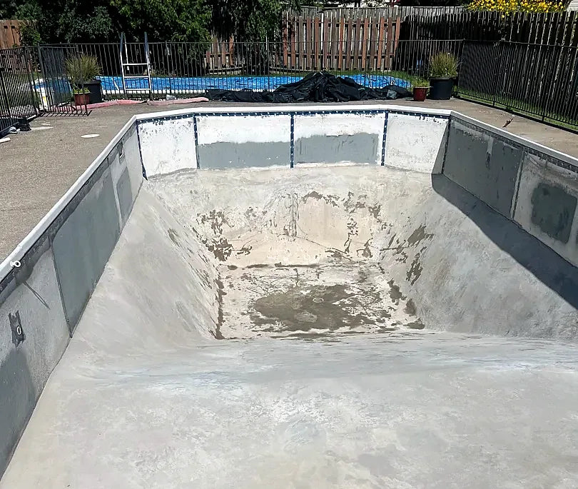 A drained pool with concrete repairs on the walls and floor
