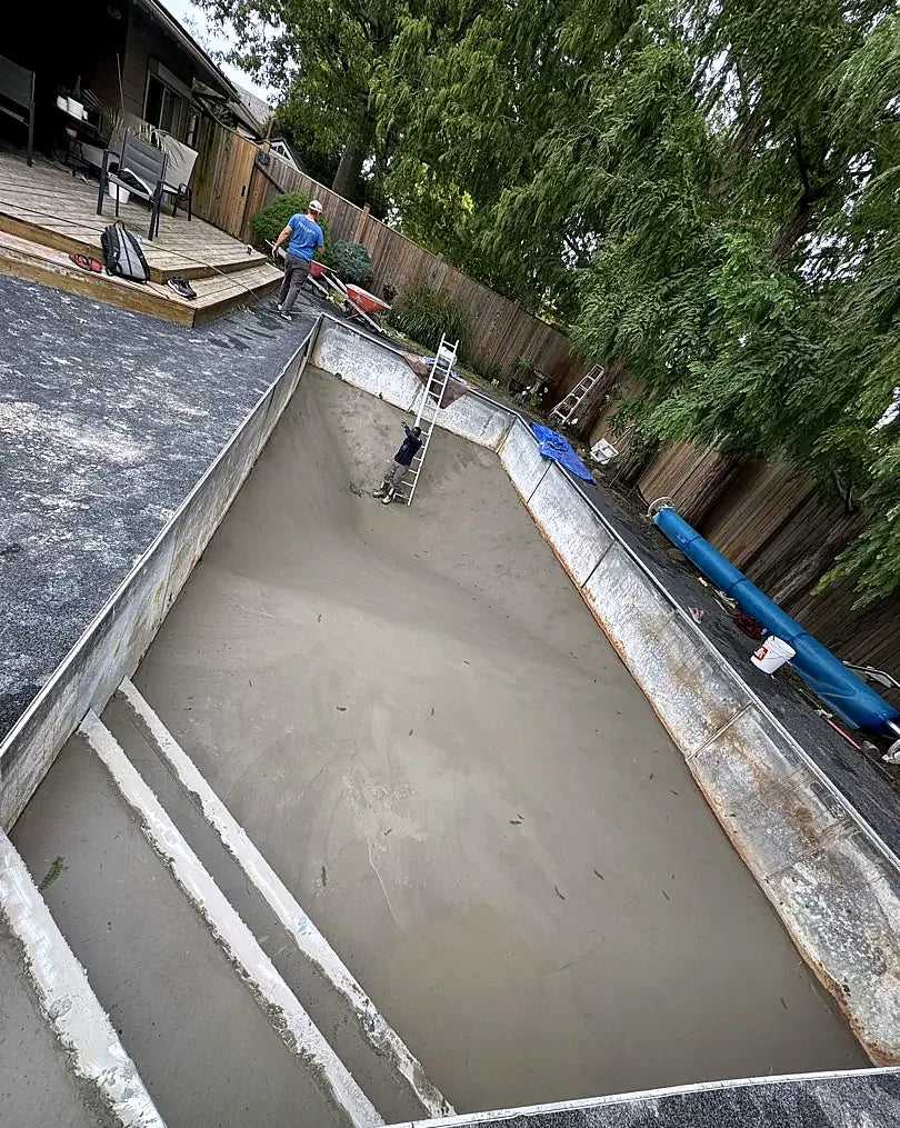 A crew working inside a drained rectangular pool with a freshly resurfaced concrete floor