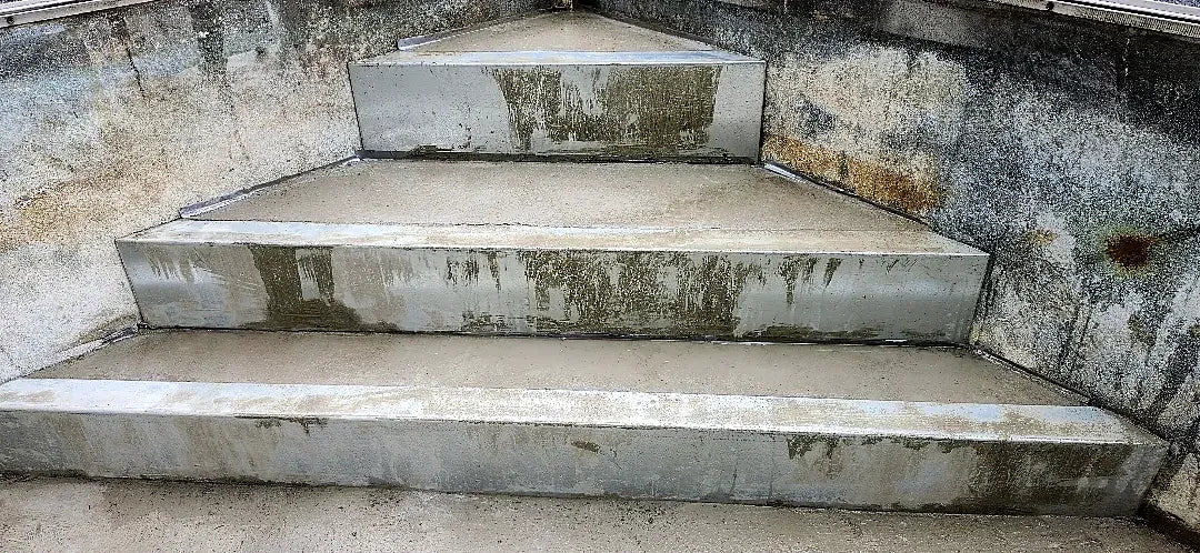 Concrete pool stairs part-way through restoration, with fresh repair mortar on the treads and risers