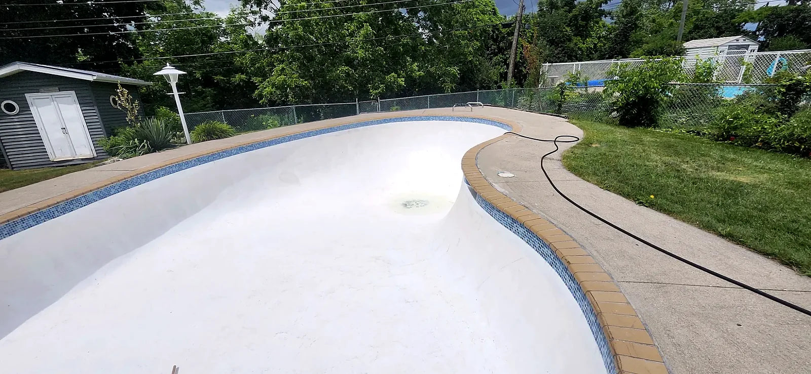 Freeform concrete pool, drained, with brick coping and a blue glass mosaic waterline band