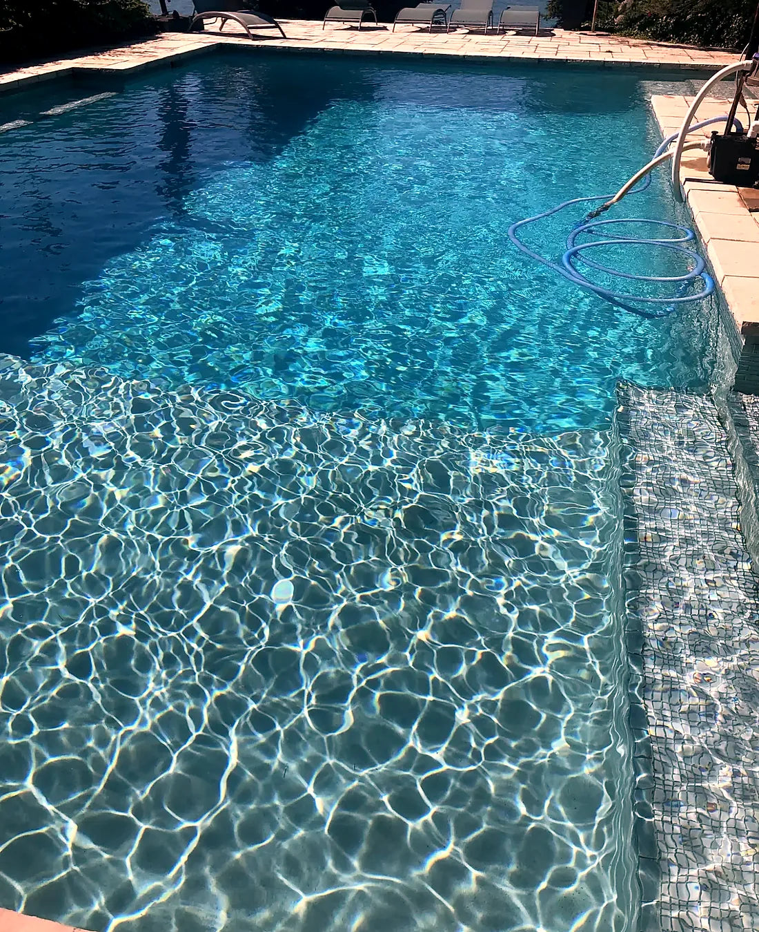 Clear pool water rippling over a freshly painted interior and mosaic-tiled step