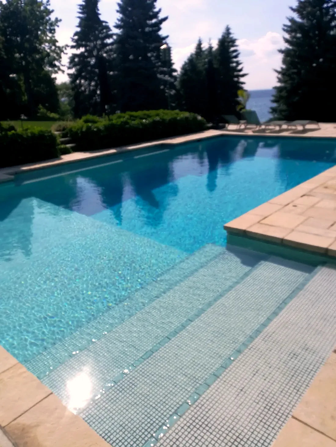 Painted concrete pool with mosaic-tiled entry steps and stone coping