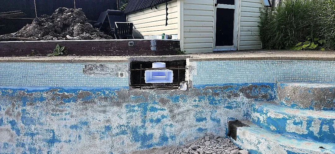 Pool wall cut open around a new skimmer, with the reinforcing steel visible