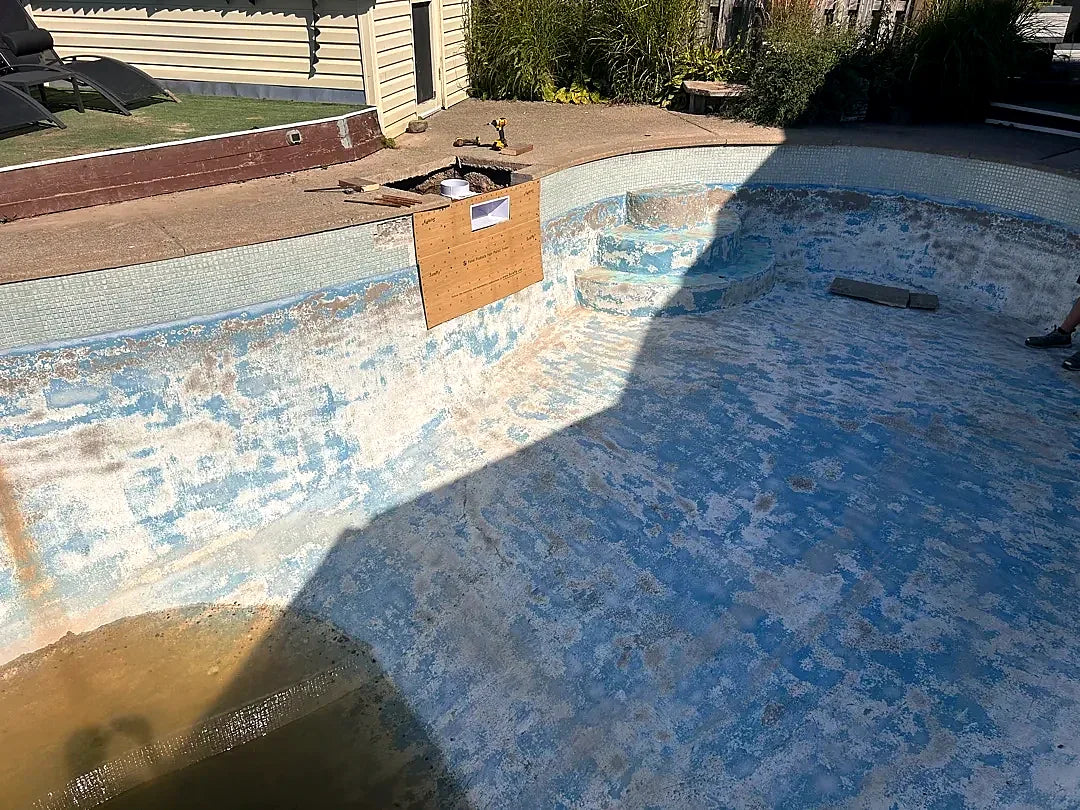 Before: a drained kidney-shaped pool with peeling blue paint