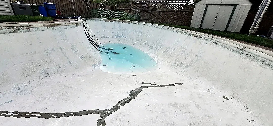 Before: a drained kidney-shaped pool with worn white paint and a long dark crack across the floor