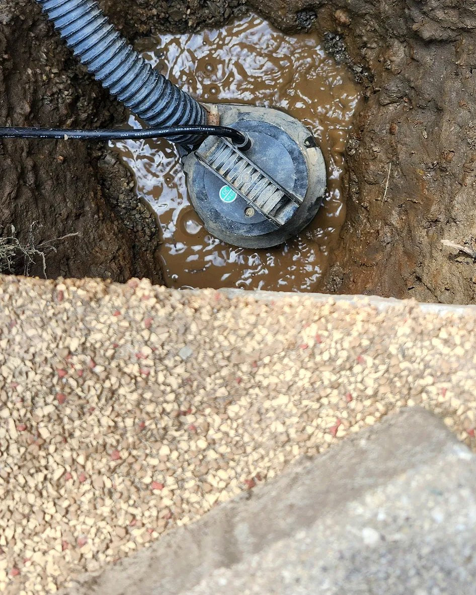 A submersible pump dewatering a muddy excavation shaft during relief-well installation, gravel backfill visible at the edge.